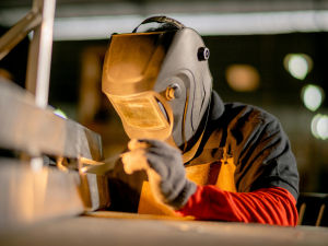 Welder using a mobile welding fume extraction unit with an extraction arm positioned near the workpiece.